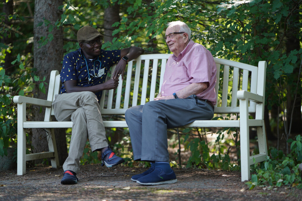 Diverse care giver, nurse sitting on park bench with elderly man