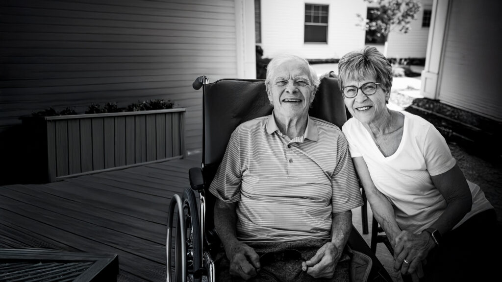 A woman sitting with a man in a wheelchair smiling.