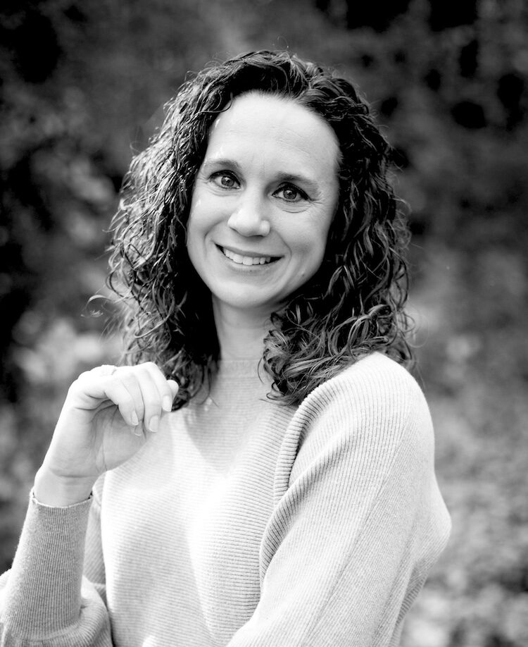 Melinda Fast, a smiling woman with curly hair in ribbed sweater, looking at camera, outdoor black-and-white portrait.