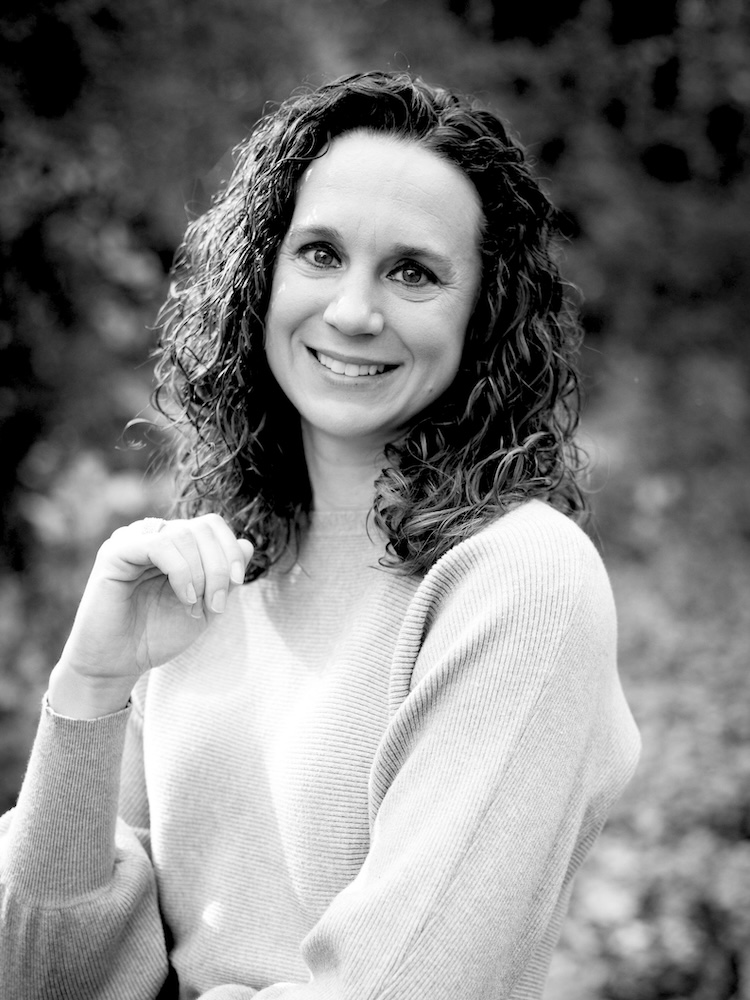 Melinda Fast, a smiling woman with curly hair in ribbed sweater, looking at camera, outdoor black-and-white portrait.