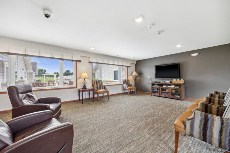 Spacious Benedict Homes living room with chairs, large windows, TV on stand, and carpeted floor.