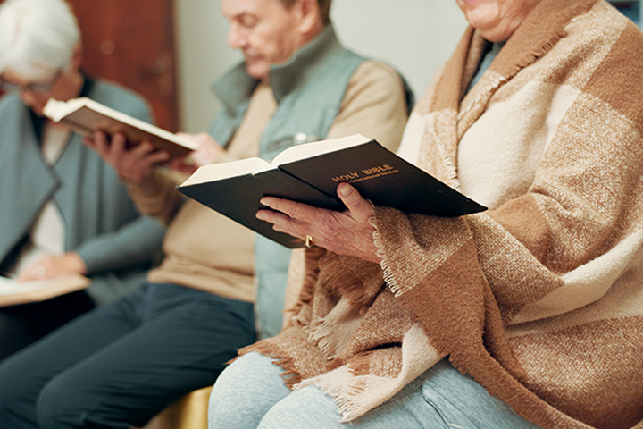 People sitting and reading books, including a person holding a Holy Bible.