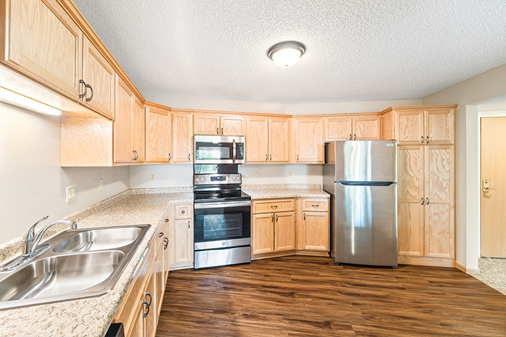 Modern kitchen with light wood cabinets, stainless steel appliances, and a double sink on granite counters.