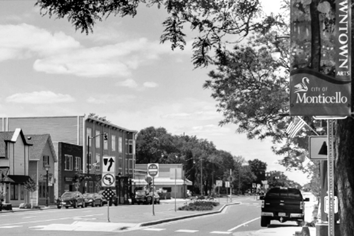 Street view of downtown Monticello, featuring lamp post signs with a swan and City of Monticello. Black and white.