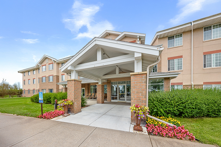 Front entrance of The Village, three-story building with large windows and landscaped greenery.