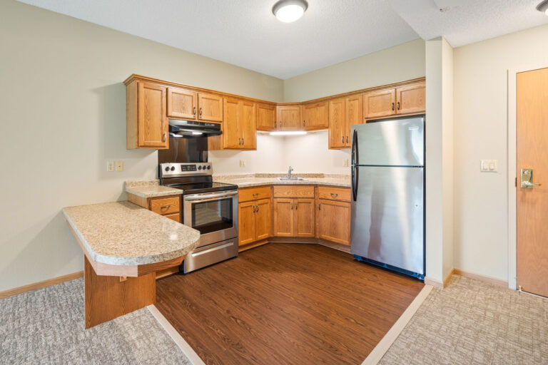 Modern kitchen in an Assisted Living Apartment with wood cabinets, stainless steel appliances, and a corner peninsula counter.