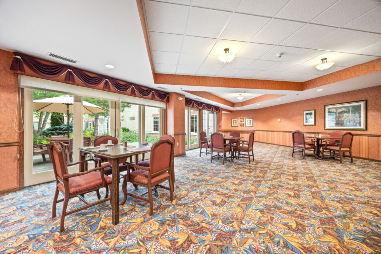A spacious dining area with tables, chairs, and large windows overlooking a garden patio with umbrellas.