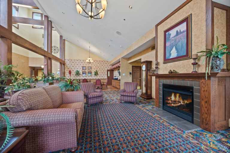 Spacious lobby with patterned carpet, cozy seating, fireplace, plants, and chandelier lighting.