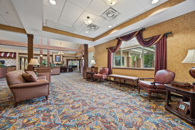 Spacious lobby with patterned carpet, brown furniture, large windows, and warm yellow walls.