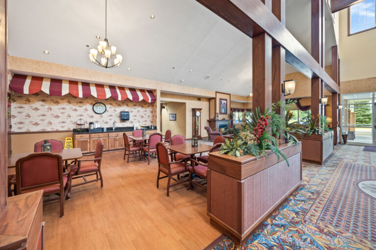 Lobby area with tables, chairs, food counter, floral carpet, and high ceilings with large windows.