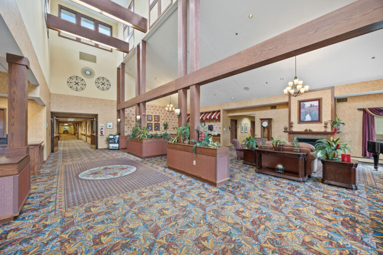 Spacious lobby with patterned carpet, tall ceilings, seating area, plants, and decorative wall art.