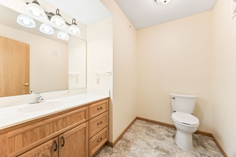 Bathroom with wooden vanity, large mirror, and toilet against cream-colored walls and tile floor.