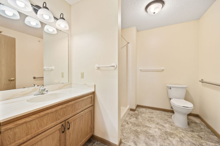 Bathroom with wooden vanity, large mirror, and toilet against cream-colored walls and tile floor.