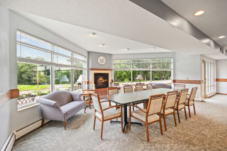 Spacious room with a long table, chairs, a couch, large windows, and a fireplace with a clock above.