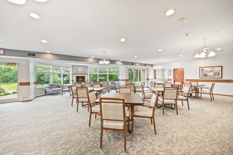 Spacious, bright independent living dining room with many tables, large windows, and neutral décor.