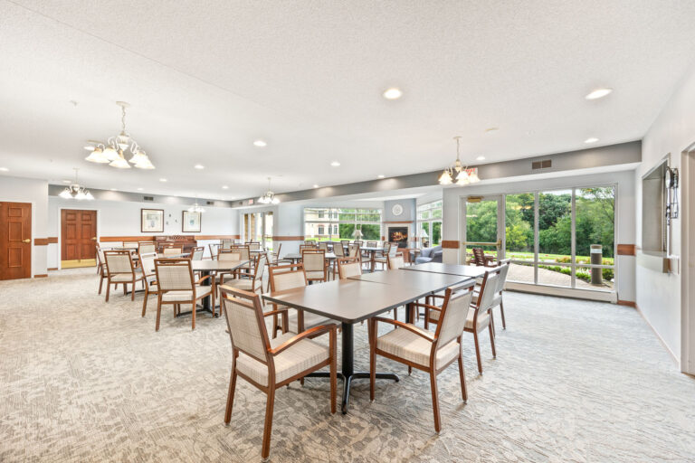Spacious, bright independent living dining room with many tables, large windows, and neutral décor.
