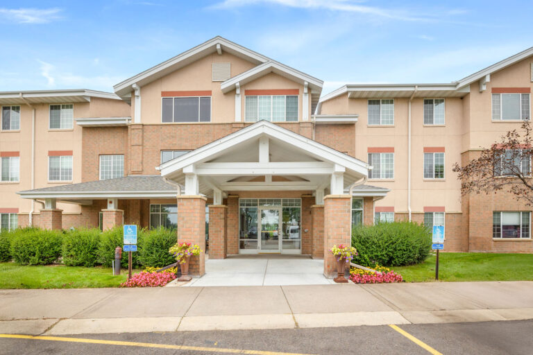 Front entrance of The Village, three-story building with large windows and landscaped greenery.