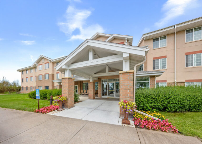 Front entrance of The Village, three-story building with large windows and landscaped greenery.