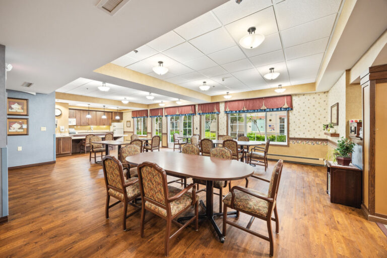 Spacious dining room with wooden floors, several tables and chairs, large windows, and bright lighting.