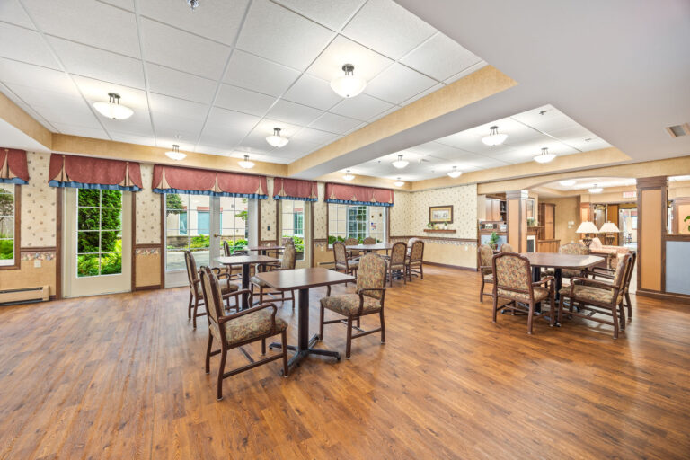 Spacious dining room with wooden floors, several tables and chairs, large windows, and bright lighting.