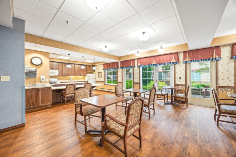 Spacious dining room with wooden floors, several tables and chairs, large windows, and bright lighting.
