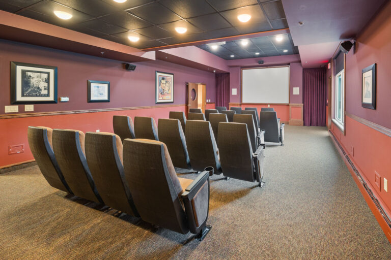 Theater room with rows of chairs, framed photos on the walls, and a large projection screen.