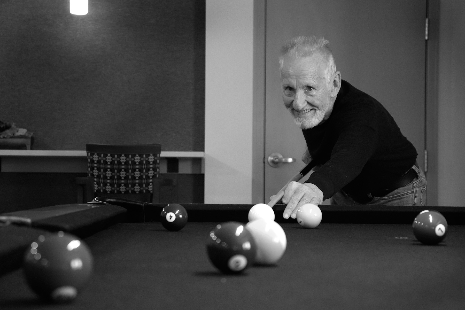 Older gentleman lining up a shot on a billiards table. Black and white.