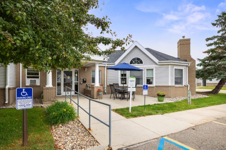 Single-story basic care 1411 building entrance with wheelchair ramp, outdoor seating, and handicap parking sign.