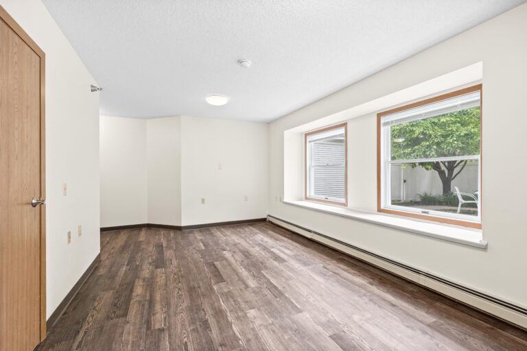 Bright living room with vaulted ceiling, fireplace, sofas, piano, and large windows letting in natural light.