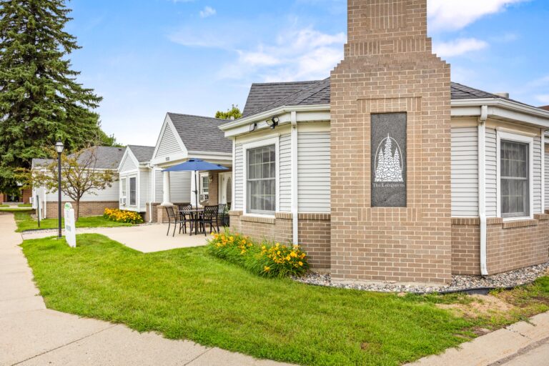 Single-story brick and siding building with a patio, outdoor furniture, and yellow flowers near the entrance.