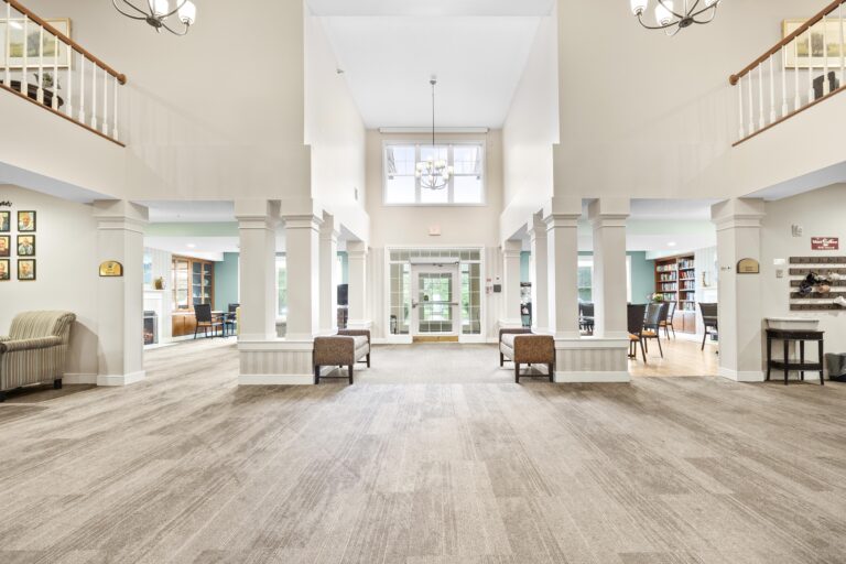 Spacious lobby with lofted ceiling, chandeliers, pillars, seating areas, and large windows letting in natural light.