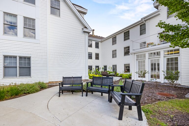 Four black benches and a table arranged on a patio in a courtyard of a white residential building.