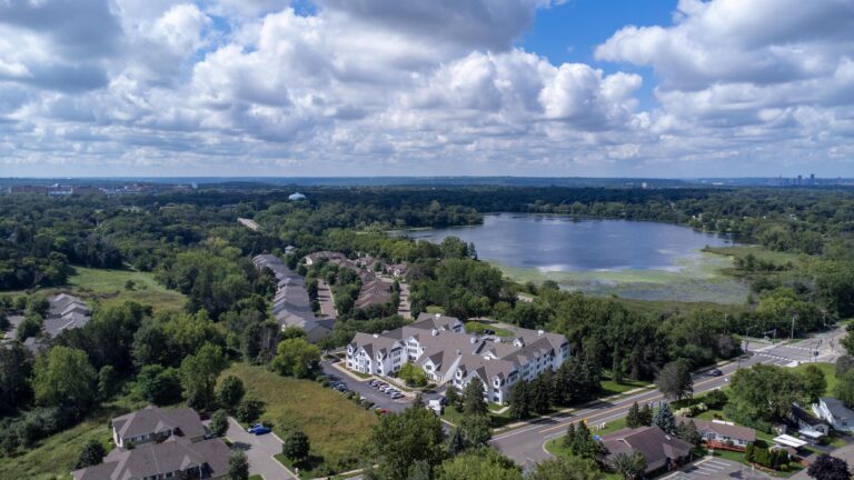 Aerial view of a residential area near a large lake surrounded by trees under a partly cloudy sky.