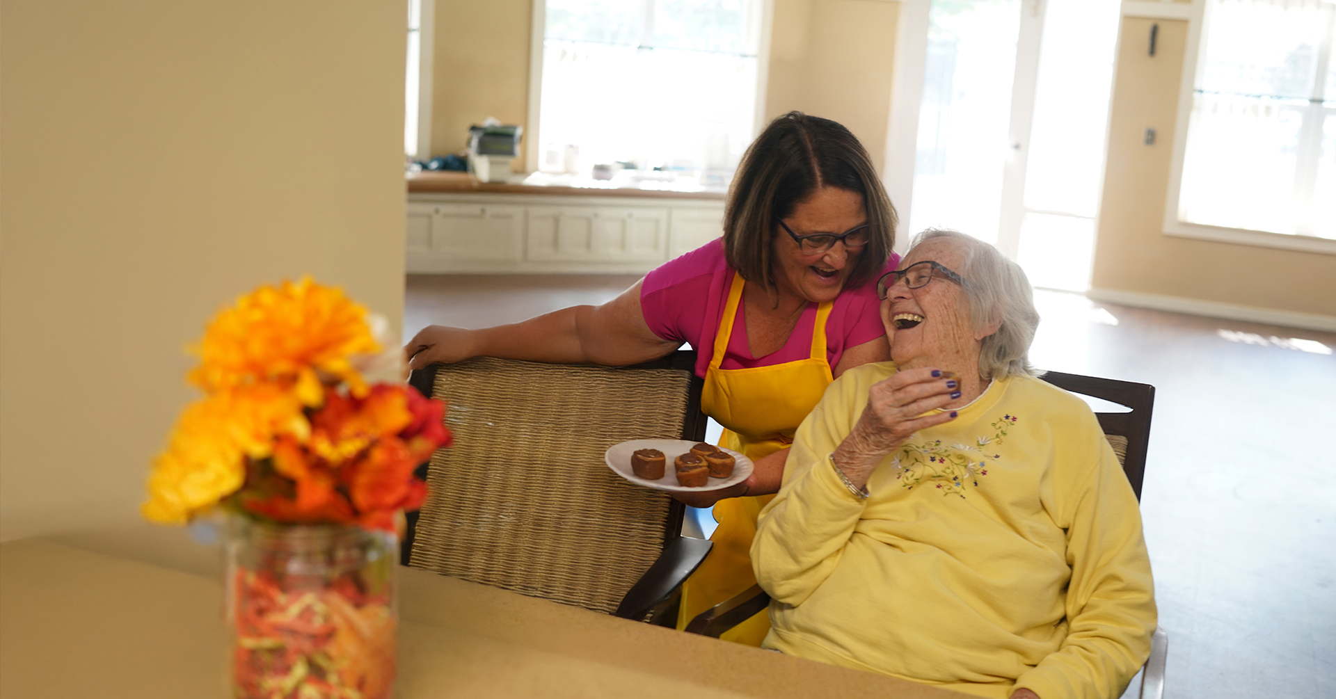 an adult female caregiver with a senior woman with dementia smiling and laughing