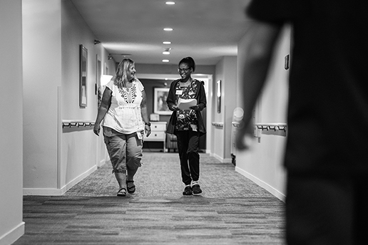 2 clinical team members walking down a hallway smiling at each other
