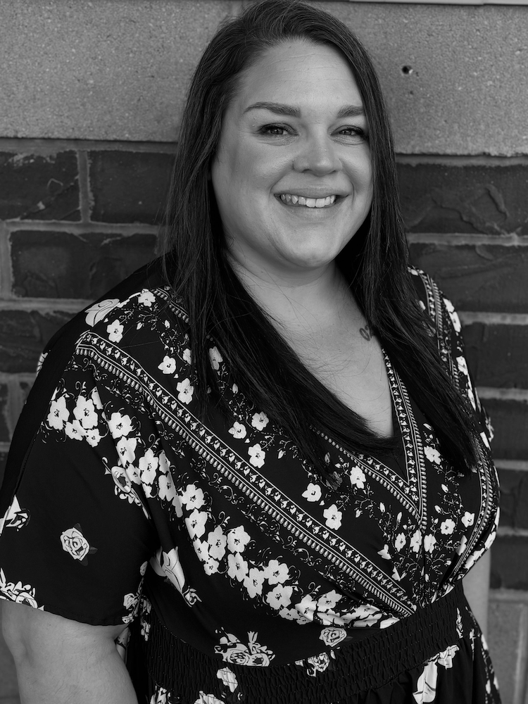 Black and white portrait of Michelle O'Connor. She wears a dark, short-sleeve blouse with a floral print.