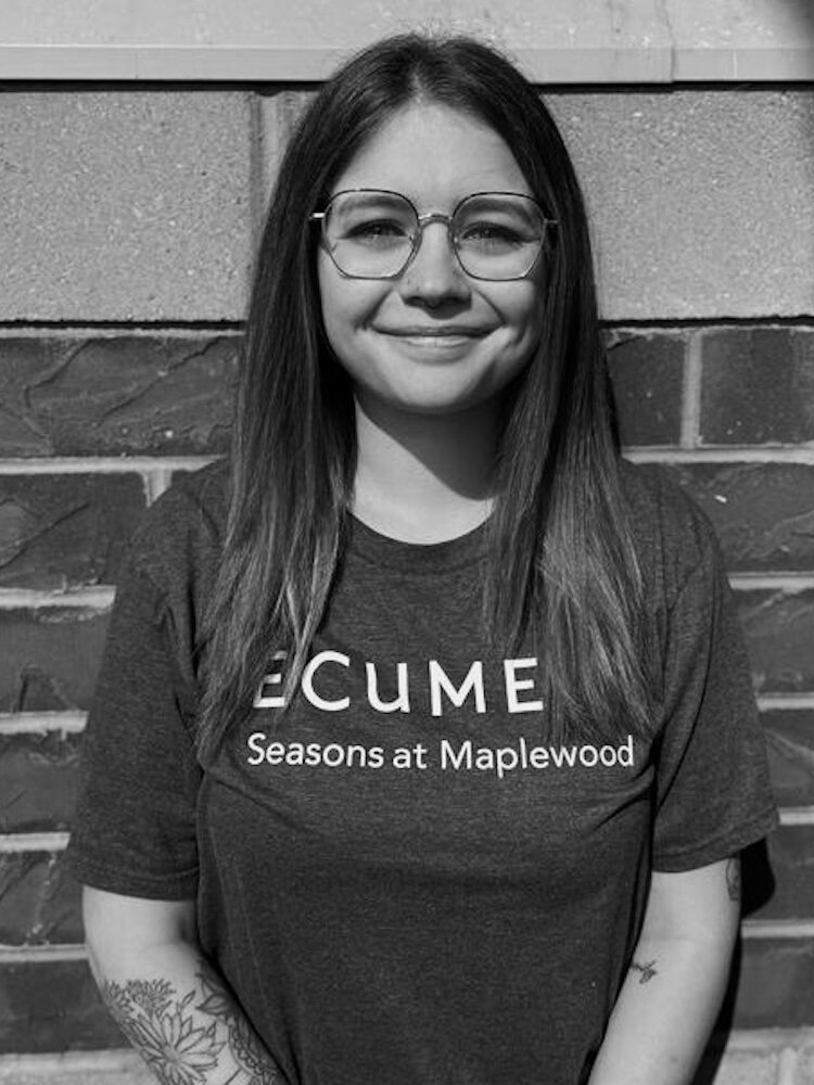 Black and white portrait of Autumn Brown. She wears eye-glasses and a t-shirt that says Eucmen Seasons at Maplewood.