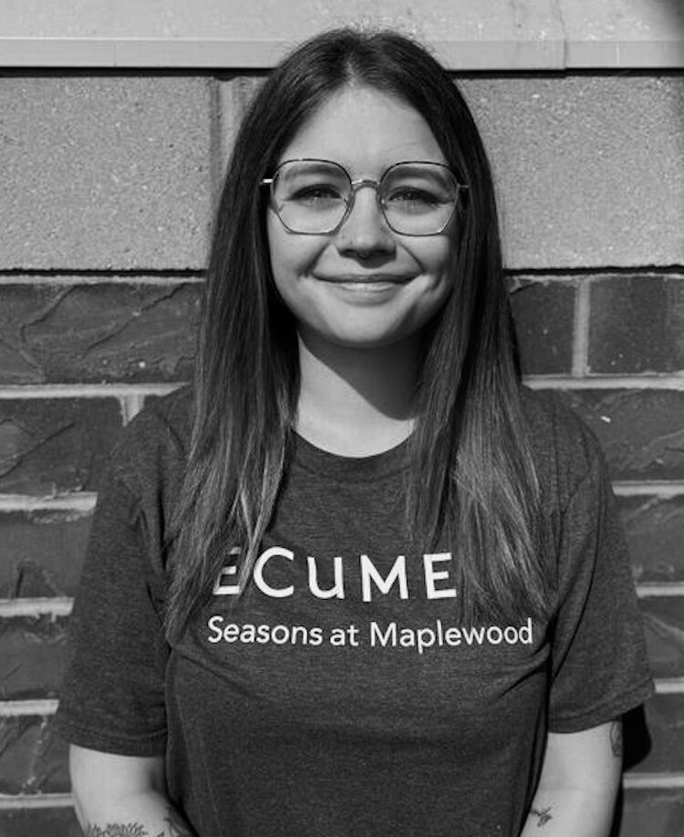 Black and white portrait of Autumn Brown. She wears eye-glasses and a t-shirt that says Eucmen Seasons at Maplewood.