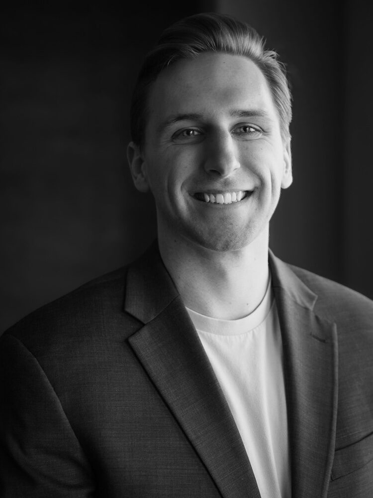 Black and white portrait of Chris Larson. He wears a dark sport coat over a light t-shirt.