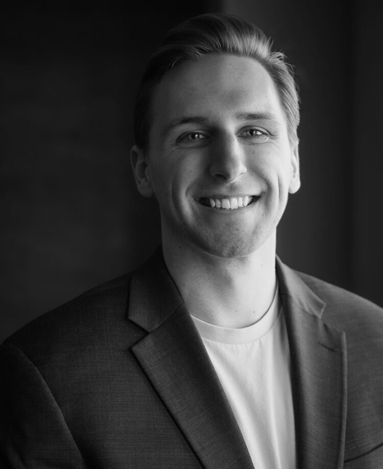 Black and white portrait of Chris Larson. He wears a dark sport coat over a light t-shirt.