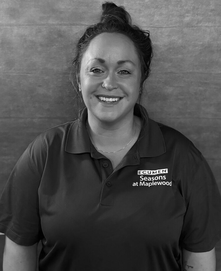 Black and white portait of Lizzi Pawlenty. She wears a dark polo shirt with an emblem that reads Ecumen Seasons at Maplewood.