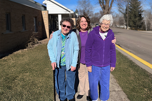 2 older adults walking outside on a sunny day with a caregiver
