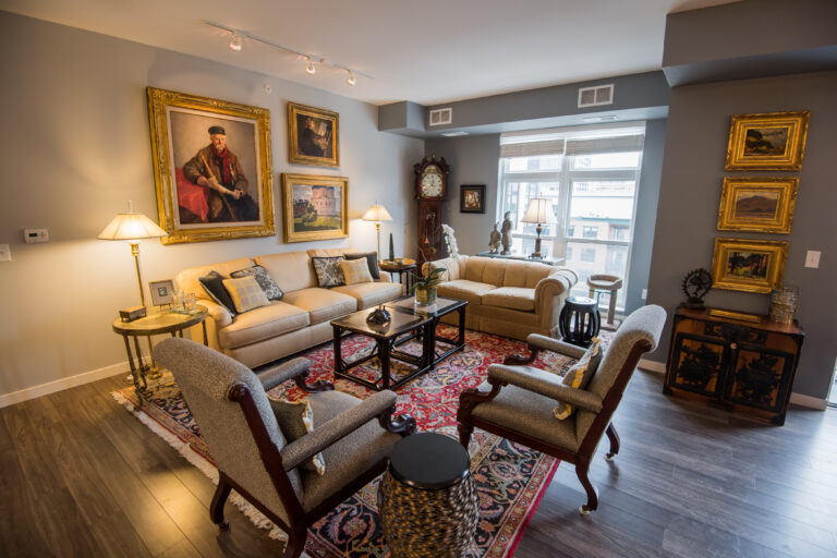 Elegant living room with classic furniture, ornate rugs, art-filled walls, and large windows with city view.