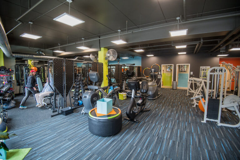 A modern gym with various exercise machines, weights, and people working out on fitness equipment.