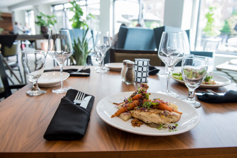 A plated chicken dish with vegetables on a set restaurant table with glasses and black napkins.