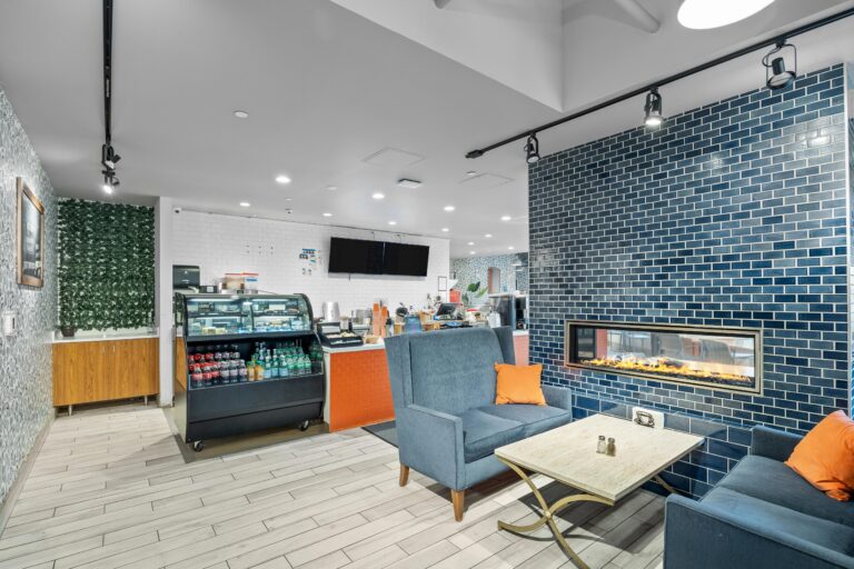 Modern café interior with blue-tiled fireplace, cozy seating, and a counter with drinks and pastries on display.