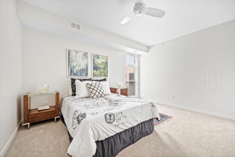 Bright bedroom with bed, two nightstands, abstract art on the wall, and a ceiling fan.