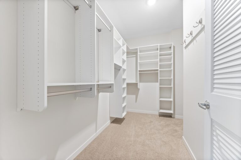 Spacious walk-in closet with white shelving, hanging rods, and beige carpeted floor.