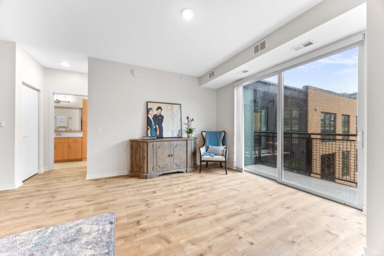 Bright living room with wood floors, a chair, sideboard, large window, and balcony view.