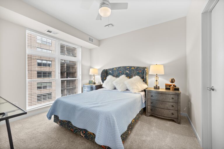 A bright bedroom with a large window, double bed, two lamps, and gray nightstands on each side.